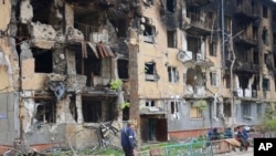 在乌克兰马里乌波尔一名男子从被炸成废墟的公寓楼前走过。（2022年5月4日）