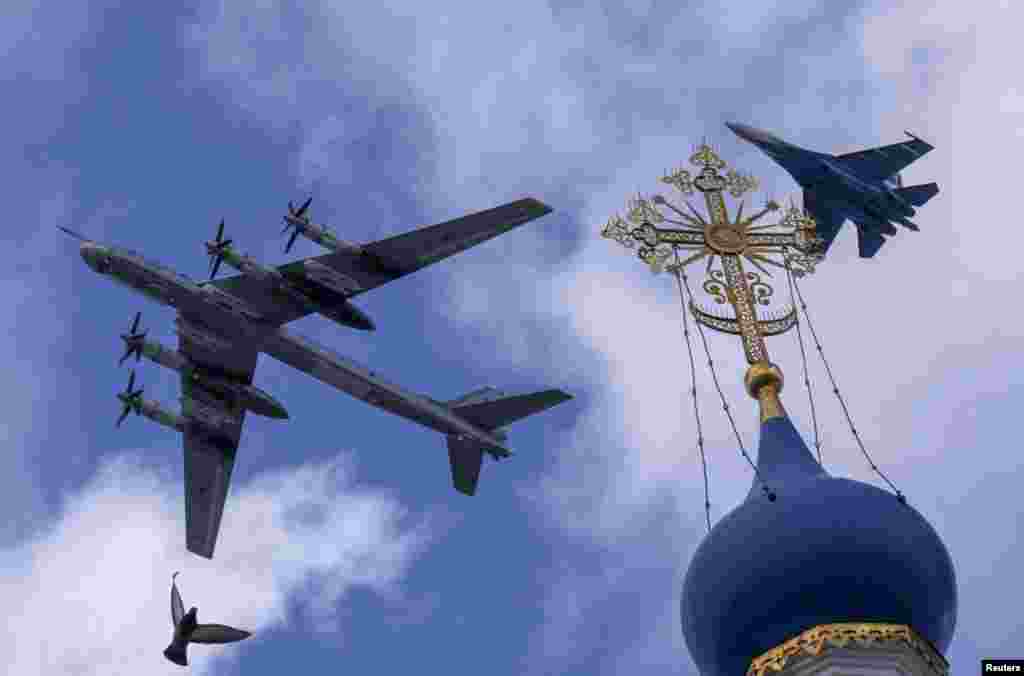 A Russian Su-35S combat aircraft and a Tu-95ms bomber fly in formation above a religious building during preparations for a military parade marking the anniversary of the victory over Nazi Germany in World War II, in Moscow.