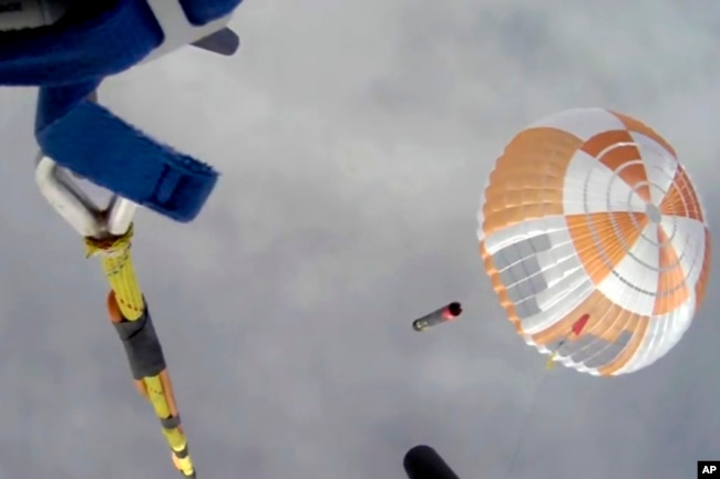 In this image made from video supplied by Rocket Lab, a helicopter hovers above as it attempts to capture Electron's first stage in mid-air by helicopter above New Zealand, Tuesday, May 3, 2022. (Rocket Lab via AP)