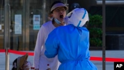 A woman opens her mouth for a swab sample during mass COVID-19 testing, in Beijing, May 3, 2022.