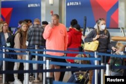 FILE - Travelers wearing masks and not wearing masks wait in line at a Delta Airlines counter, at Logan International Airport in Boston, Massachusetts, April 19, 2022.