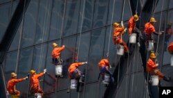 Workers wearing face masks hang from ropes as they wash windows on the China Central Television (CCTV) building in Beijing, May 4, 2022. Beijing on Wednesday closed around 10% of the stations in its vast subway system in an effort to curb the spread of COVID-19.