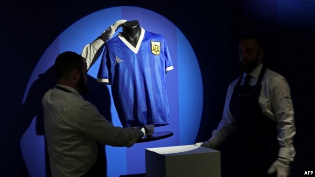 In this file photo taken in London on April 20, 2022 Sotheby's technicians adjust a shirt worn by Argentina's Diego Maradona during the 1986 World Cup quarterfinal match against England.