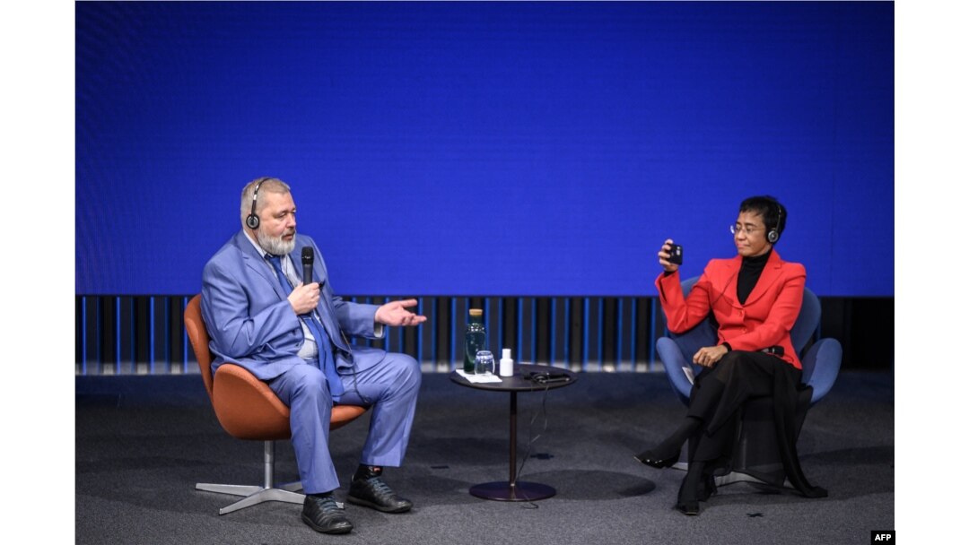 Nobel Peace Prize laureate Maria Ressa, right, films with her mobile Nobel Peace Prize laureate Dmitry Muratov as he speaks during World Press Freedom Day in Geneva, May 3, 2022.