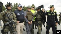 En esta foto publicada por la Oficina de Prensa de la Presidencia de Colombia, la escolta policial de Dairo Antonio Usuga, centro, también conocido como "Otoniel", líder del violento cartel Clan del Golfo antes de su extradición a EEUU. en un aeropuerto militar en Bogotá.