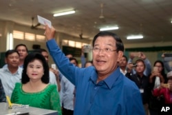 FILE - Cambodian Prime Minister Hun Sen of the Cambodian People's Party shows off his ballot paper next to his wife, Bun Rany, foreground left, before voting in local elections at Takhmau polling station in Kandal province, June 4, 2017.