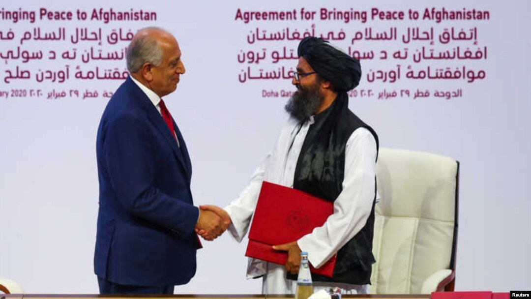 El delegado estadounidense Zalmay Khalilzad y Mulah Abdul Ghani Baradar, líder de la delegación talibana, se estrechan las manos tras firmar un acuerdo en Catar el 20 de febrero.