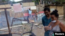 Personas cocinan con leña mientras una mujer trabaja en una casa hecha con barro, palos y láminas de hojalata, en un terreno baldío en el municipio de Sucre, cerca de Caracas, Venezuela el 12 de junio. 2020. Foto tomada el 12 de junio de 2020. REUTERS/Manaure Quintero