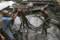 FILE - Fishermen sort out their fishing net at the bank of a polluted river in Bidere community in Ogoniland in Nigeria's delta region, Aug. 20, 2011.