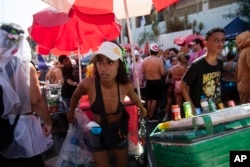 A vendor pulls through a crowd of revelers a cart carrying a cooler of ice cold beverages at the Heaven on Earth pre-Carnival street party, in Rio de Janeiro, Feb. 22, 2025.