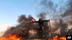 An anti-government protester jumps over burning tires blocking a street during a demonstration against newly-appointed Prime Minister Mohammed Allawi, in Najaf, Iraq, Feb. 2, 2020. 