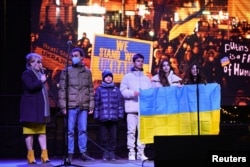 Hassan Al-Khalaf, 11, who escaped from Ukraine to Slovakia on his own, stands on stage with family members as they hold a Ukrainian national flag during an anti-war rally, following Russia's invasion of Ukraine, in Bratislava, Slovakia, March 11, 2022.