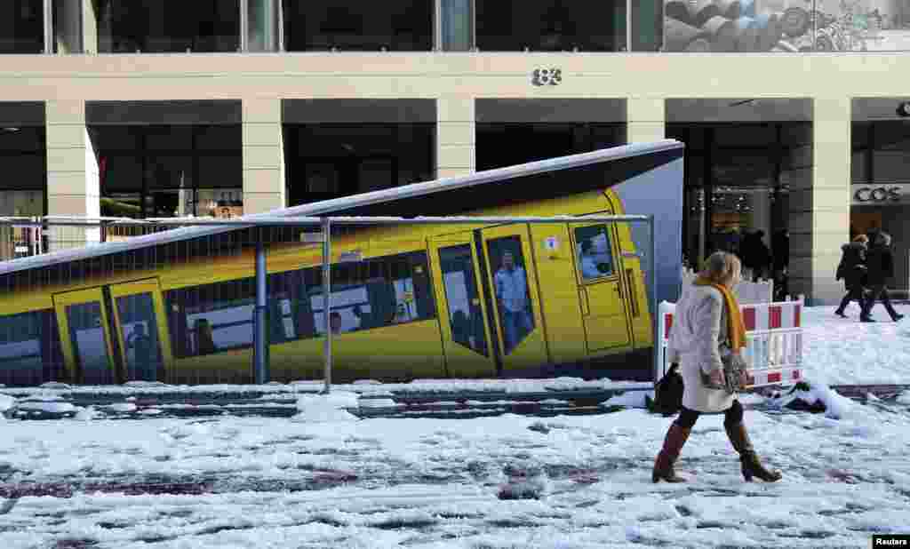 People walk beside a painted U-Bahn underground train marking an entrance of the new Unter den Linden underground station currently under construction in Berlin, Germany.