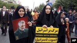 FILE - Iranian women, one of them holding an anti-Israeli placard, attend a pro-Palestinian rally, in Tehran, Iran, Oct. 13, 2023. The woman at left holds a portrait of the late Iranian Revolutionary Guard Gen. Qassem Soleimani, who was killed in a U.S. drone attack in 2020.