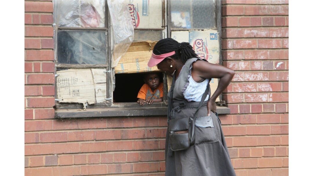 A woman talks to a child through a window in Harare, May 28, 2020. Manhunts have begun after hundreds of people, some with the coronavirus, fled quarantine centers in Zimbabwe and Malawi.