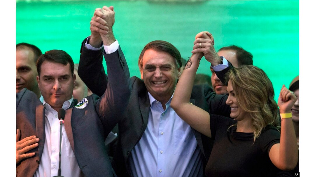El candidato presidencial de Brasil, Jair Bolsonaro, en el centro, levanta la mano a su esposa Michelle y su hijo Flavio ante sus partidarios durante la convención del Partido Nacional Social Liberal, donde aceptó la candidatura del partido. Julio 22 de 2018.