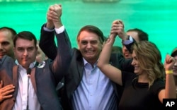 El candidato presidencial de Brasil, Jair Bolsonaro, en el centro, levanta la mano a su esposa Michelle y su hijo Flavio ante sus partidarios durante la convención del Partido Nacional Social Liberal, donde aceptó la candidatura del partido. Julio 22 de 2018.