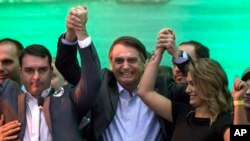 ARCHIVO - En esta foto del 22 de julio de 2018, el candidato presidencial brasileño Jair Bolsonaro (centro), toma de la mano a su esposa Michelle y su hijo Flavio durante la convención del Partido Nacional Social Liberal donde aceptó la nominación del partido en Río de Janeiro, Brasil. El candidato presidencial de extrema derecha anunció el domingo 5 de agosto de 2018 que eligió al general de reserva del ejército Hamilton Mourao como compañero de fórmula para las próximas elecciones generales de Brasil en octubre. (Foto AP / Leo Correa, Archivo)