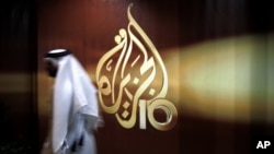 FILE - A Qatari employee of Al Jazeera Arabic language TV news channel walks past the network's logo, in Doha, Qatar, Nov. 1, 2006.