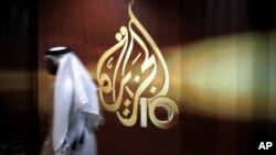 FILE - A Qatari employee of Al Jazeera Arabic language TV news channel walks past the logo of Al Jazeera in Doha, Qatar,