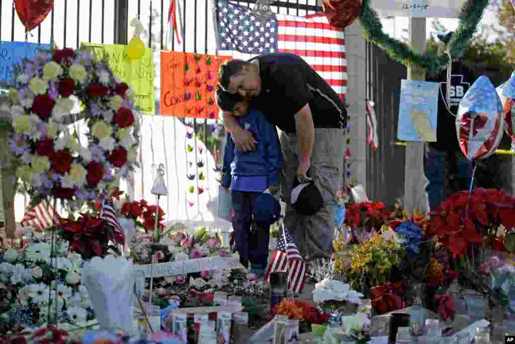 Gary Mendoza, and his son Michael pay their respects at a makeshift memorial site honoring shooting victims in San Bernardino, California. Thousands of employees of San Bernardino County are preparing to return to work, five days after a county restaurant inspector and his wife opened fire on a gathering of his co-workers, killing 14 people and wounding 21.