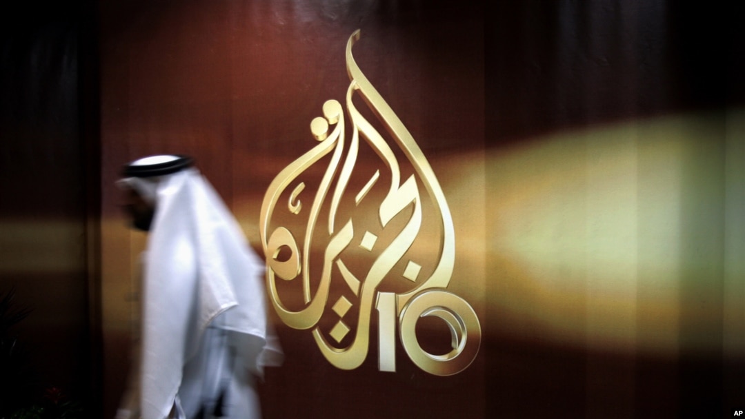 FILE - A Qatari employee of Al Jazeera Arabic language TV news channel walks past the logo of Al Jazeera in Doha, Qatar,