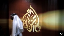 FILE - A Qatari employee of Al Jazeera Arabic language TV news channel walks past the logo of Al Jazeera in Doha, Qatar,