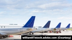 FILE - The tails of airplanes sitting at gates to an airport.