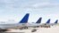 FILE - The tails of airplanes sitting at gates to an airport.
