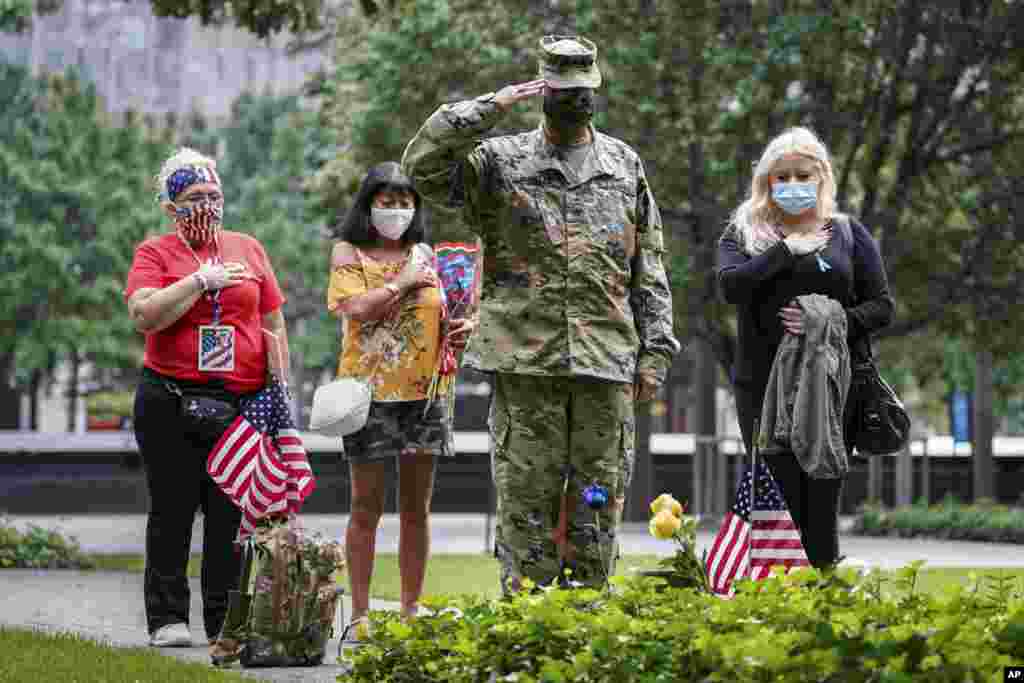 US Army Sgt. Edwin Morales, center right, salutes after places flowers for fallen FDNY firefighter Ruben D. Correa at the National September 11 Memorial and Museum, Friday, Sept. 11, 2020, in New York. The names of nearly 3,000 victims of the Sept. 11, 2001 terror attacks will be read by family members at a ceremony organized by the Tunnel to Towers Foundation. (AP Photo/John Minchillo)