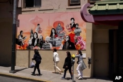 A group of women walk up Jackson Street in Chinatown past the new "AAPI Community Heroes" mural in San Francisco, Monday, May 23, 2022. (AP Photo/Eric Risberg)