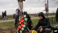 FILE - Yura Nechyporenko, 15, places a chocolate at the grave of his father Ruslan Nechyporenko at the cemetery in Bucha, on the outskirts of Kyiv, Ukraine, on April 21, 2022. 