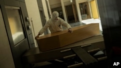 FILE - A worker, wearing full protective gear, moves the casket of a victim of COVID-19 to be cremated during a partial lockdown to prevent the spread of coronavirus at the Pontes crematorium center in Lommel, Belgium, Thursday, April 16, 2020. (AP Photo/Francisco Seco, File)