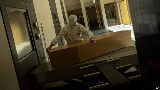 FILE - A worker, wearing full protective gear, moves the casket of a victim of COVID-19 to be cremated during a partial lockdown to prevent the spread of coronavirus at the Pontes crematorium center in Lommel, Belgium, Thursday, April 16, 2020. (AP Photo/Francisco Seco, File)