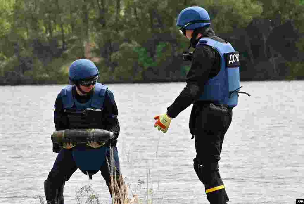 Dua penjinak ranjau Ukraina mengumpulkan bahan yang tidak meledak selama pekerjaan mengamankan ranjau di Danau Biru di desa Horenka, wilayah Kyiv, menjelang musim mandi yang semakin dekat. (Foto: AFP)