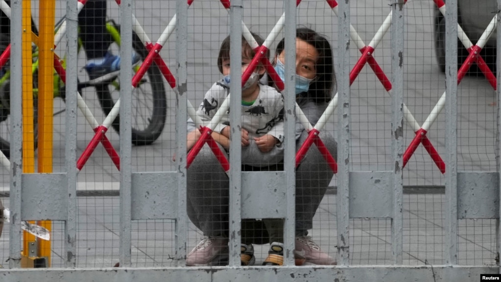 上海封城，一名女子和一个幼童从被封闭的居民小区栅栏后向外张望。（2022年5月10日）(photo:VOA)