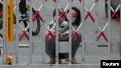 A resident and a child look out through gaps in the barriers at a closed residential area during lockdown, amid the COVID-19 pandemic, in Shanghai, China, May 10, 2022. 