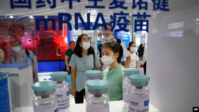 FILE - Visitors look at giant replica bottles of COVID-19 vaccine produced by Sinopharm subsidiary CNBG using mRNA technologies at the China International Fair for Trade in Services in Beijing, China, Sept. 5, 2021.