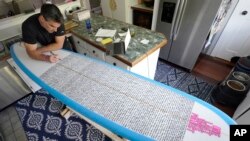 Dan Fischer uses a paint marker to place names of people's lost loved ones on one of his surfboards at his home, in Newport, Rhode Island, May 25, 2022.