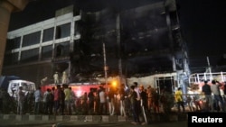 Rescue workers and onlookers stand as crews douse a fire that broke out at a commercial building in Delhi's western suburb of Mundka, May 13, 2022.