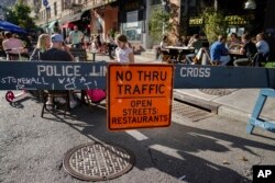 Para pelanggan duduk di luar restoran yang mengoperasikan ruangan di luar serta tersebar hingga ke trotoar dan jalan saat pandemi COVID-di New York.