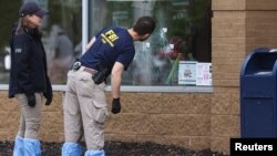 Anggota FBI tampak mengamati lubang pada kaca yang tertembak peluru di lokasi penembakan di supermarket Tops di Buffalo, New York, pada 16 Mei 2022. (Foto: Reuters/Brendan McDermid)