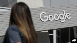 FILE - A woman walks below a Google sign on the campus in Mountain View, Calif., on Sept. 24, 2019.