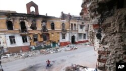 Niños caminan entre edificios destruidos durante los combates en Mariúpol, en territorio bajo el gobierno de la autodenominada República Popular de Donetsk, en el este de Ucrania, el 25 de mayo de 2022.