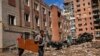 Two men carry a wood panel next to damaged buildings and destroyed cars in a Russian bombing in Bakhmut, eastern Ukraine, May 24, 2022. The town of has been coming under increasing artillery strikes over the last week as Russian forces try to encircle the city of Sieverodonetsk.