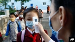 FILE - A teacher takes the body temperature of a schoolgirl to help curb the spread of the coronavirus before entering Kim Song Ju Primary School in Central District in Pyongyang, North Korea, on Oct. 13, 2021.