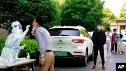 En esta foto divulgada por la agencia de noticias china china Xinhua, residentes de Shanghái hacen fila para someterse a una prueba de COVID-19 el 17 de mayo de 2022.