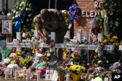A state trooper places a tiara on a cross honoring Ellie Garcia, one of the victims of the elementary school shooting in Uvalde, Texas, May 28, 2022.