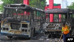 A worker sweeps the street alongside the burnt buses near Sri Lanka's former prime minister Mahinda Rajapaksa's official residence, a day protests in Colombo, Sri Lanka.