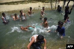 Para pemuda mendinginkan diri di danau kecil saat musim panas yang terik di Karachi pada 14 Mei 2022. (Foto: AFP)